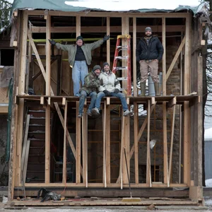 Four volunteers waving from inside the wood-framed shell of The Crooked House during construction
