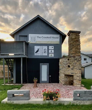 The completed Crooked House sculpture at sunset with sponsor banners on its black facade