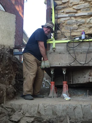 A worker steadying jack supports at the base of the stone chimney during foundation work