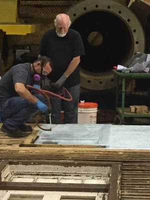 Two volunteers sealing a concrete panel in the fabrication shop