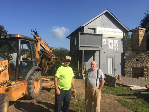 Two volunteers standing in front of the sculpture with a backhoe during groundwork