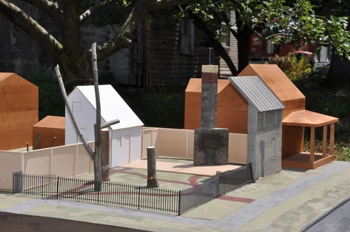 Architectural foam-board model of The Crooked House showing the white facade, fence, and stone chimney