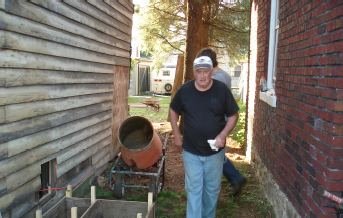 A volunteer working with a wheelbarrow of cement alongside the brick alley