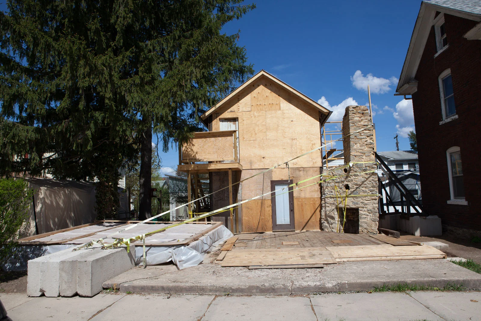 The Crooked House under construction, with plywood-clad facade and the stone chimney in place